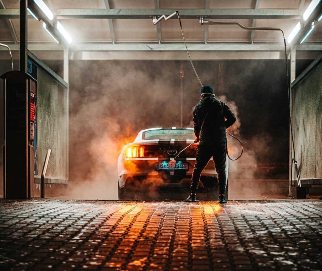 A person washing a sports car at a carwash during the night, illuminated by lights.