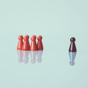 Red game pieces grouped with one isolated piece symbolizing social distancing on a reflective surface.